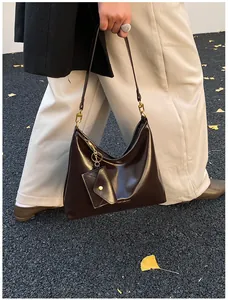 Detail der dunkelbraunen, glänzenden Hobo-Tasche mit Goldbeschlägen und kleiner Tasche