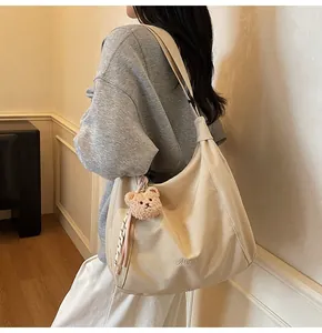 Détail d'un grand sac hobo beige avec pendentif ours porté par un mannequin en intérieur
