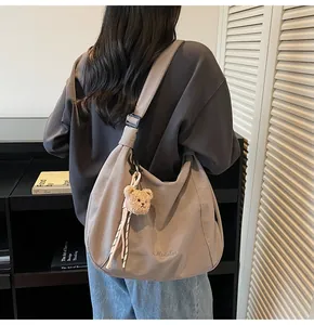 Détail d'un sac demi-lune en toile grise avec bandoulière réglable et breloque ours