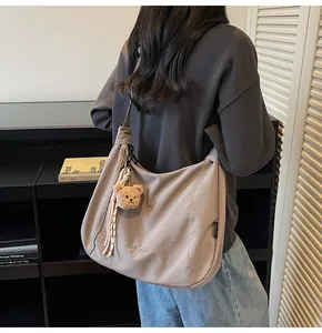 Détail du sac demi-lune en toile grise avec broderie et pendentif ours en peluche marron