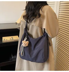 Détail du sac hobo en toile bleu foncé avec breloque ours sur un trench-coat kaki