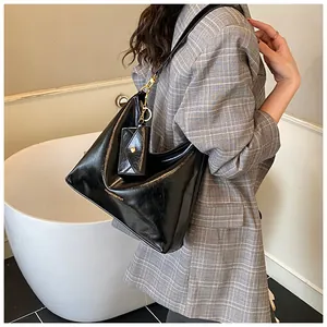 Schwarze glänzende Leder-Hobo-Tasche mit Mini-Umschlagtasche am Model in minimalem Setting