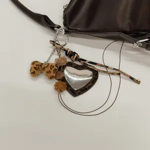 Détail d'un porte-clés à nœud léopard avec miroir en cœur sur un sac à main en cuir brun