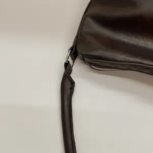 Gros plan du sac en cuir marron foncé avec anneaux argentés et détails de fermeture