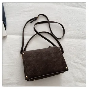 Macro shot of dark brown square bag showing retro leather texture and golden rivets detail