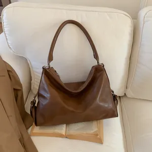 Sac fourre-tout rétro en cuir marron sur canapé blanc avec trench et livre