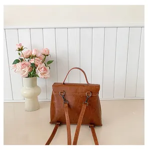 Detail eines braunen Vintage-Rucksacks mit Griff und verstellbaren Trägern auf weißem Holz