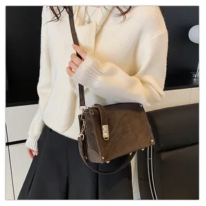Close-up of deep brown textured leather crossbody bag with gold metal clasp and studs