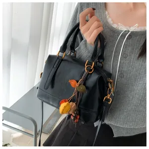 Detailed view of black Boston bag with gold rings and a colorful leaf leather charm