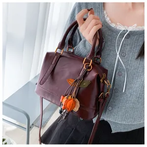 Close-up of a retro dark red Boston pillow bag with a colorful leaf charm and gold hardware