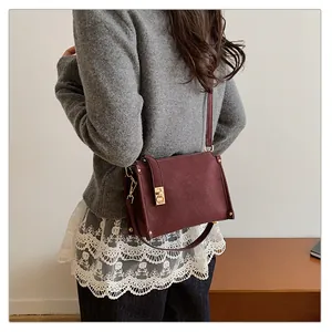 Close-up of a burgundy square shoulder bag with gold clasp worn by a female model