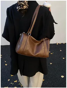 Détail d'un sac Boston en similicuir marron foncé porté par un mannequin en manteau noir