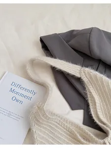 Detail showing the plush knitted texture of the beige shoulder bag over a grey suit