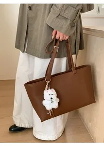 Detail of dark brown faux leather tote bag with plush puppy charm on adjustable handles