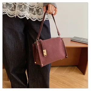 Retro burgundy square bag with gold rivets and metallic twist lock on model's shoulder