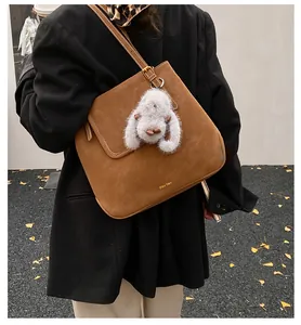 Brown suede tote bag detail with white plush rabbit charm on a model in black coat