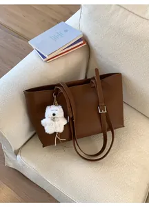Detail of a dark brown PU leather tote bag with a plush puppy charm on a white sofa