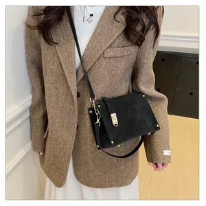 Close-up of black crossbody square bag with gold hardware and rivet details on brown blazer
