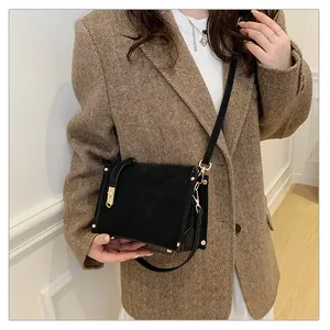 Close-up of black crossbody bag with gold lock on a brown herringbone blazer