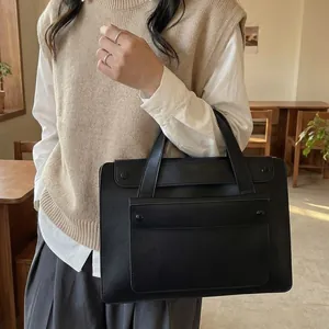 Minimalist black waterproof business tote bag with front pocket shown in a cafe setting