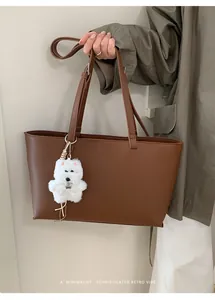 Brown leather tote bag with a white plush puppy charm held by a model in a trench coat