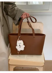 Detail of coffee brown PU leather tote bag with white puppy charm on a wooden chair