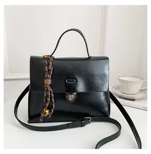 Detail der schwarzen Lackleder-Handtasche mit Silberverschluss und gewebtem Anhänger