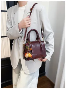 Detail of burgundy leather boston bag with a leaf charm accessory worn cross-body
