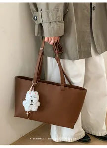 Detail of dark brown faux leather tote bag with grainy texture and plush puppy charm