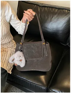 Close-up of matte bucket bag with golden hardware and plush rabbit keychain on leather sofa