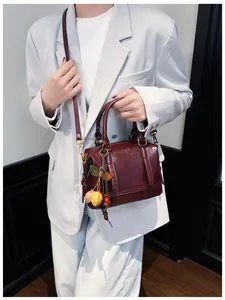 Detail of burgundy leather Boston bag with vintage floral charm on a white blazer