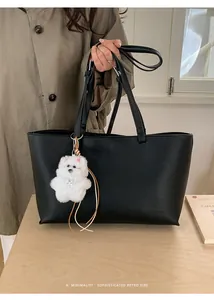 Detail of a black leather tote bag with a white plush dog pendant and minimalist handle