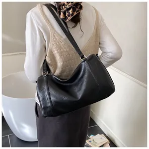 Détail d'un sac à bandoulière en cuir noir brillant porté par un mannequin