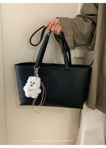 Close-up of black PU leather tote bag with a cute white plush puppy pendant detail