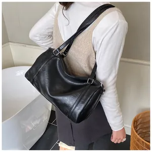 Vue détaillée d'un sac Boston cylindrique en cuir noir porté à l'épaule avec zip métal