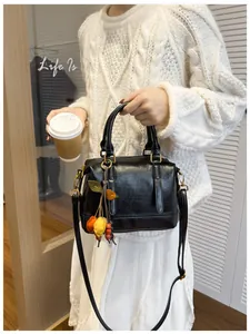 Close-up of black leather Boston bag with colorful fruit pendant and slim shoulder strap