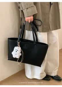 Detail of black leather tote bag with grainy texture and a cute white puppy plush charm
