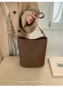 Detail of a brown lychee-textured bucket bag held by a model in a minimalist setting