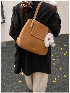 Detail of caramel brown suede tote bag with a white plush rabbit charm on a street