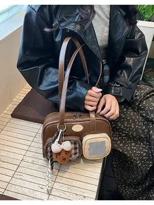 Détail du sac bandoulière marron avec poches texturées et un pendentif ours en peluche