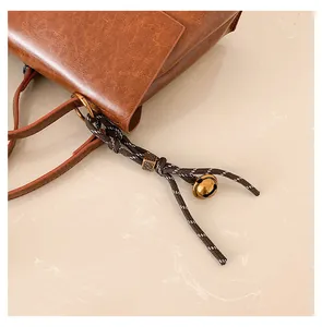 Detail der braunen Ledertasche mit geflochtener Quaste und goldenem Glockenanhänger
