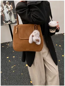 Caramel suede bucket bag with plush rabbit charm shown in a stylish urban street setting