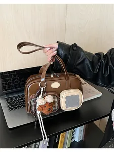 Détail du sac polochon marron avec poches extérieures et breloque ours en peluche