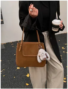 Brown faux suede bucket bag shown with a plush rabbit charm in an autumn urban setting