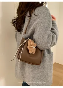 Détail d'un sac seau rétro en cuir marron avec un ourson en peluche et un cordon sur la fermeture