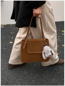 Brown suede bucket tote bag with a plush bunny charm shown in an outdoor street setting