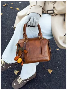 Detail of a brown leather Boston bag with leaf charms held by a model in autumn street style