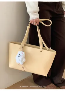 Detail of beige lychee grain leather tote bag with white plush dog pendant on shoulder