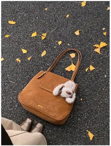 Brown suede tote bag detail with plush rabbit charm on autumn ginkgo leaves ground