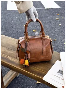 Detail of vintage brown Boston bag with leaf fruit charm on a wooden bench outdoors